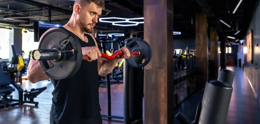 Young athletic man swinging his arms with a barbell in the gym. Sport lifestyle. . High quality photo