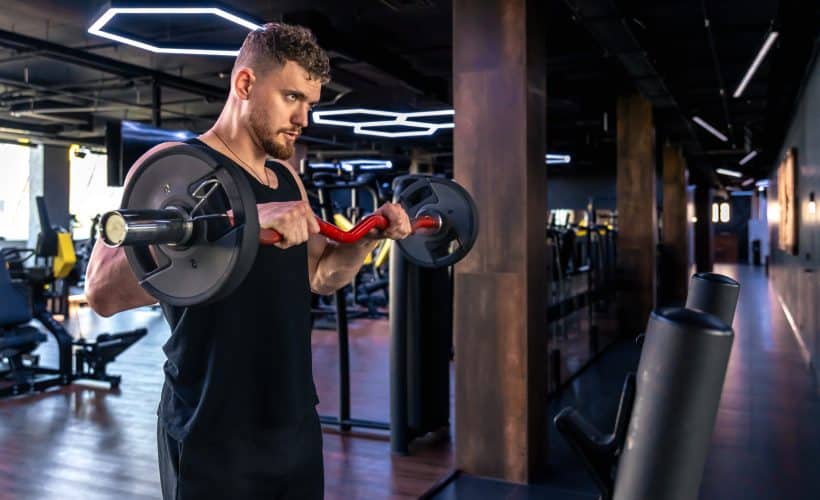 Young athletic man swinging his arms with a barbell in the gym. Sport lifestyle. . High quality photo