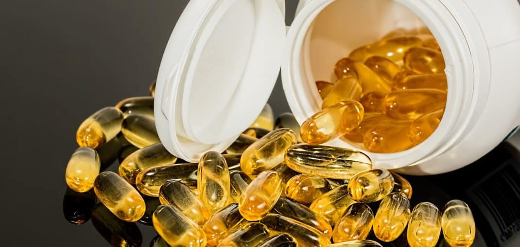 Close-up view of a spilled container of golden capsules or pills, likely dietary supplements or vitamins.