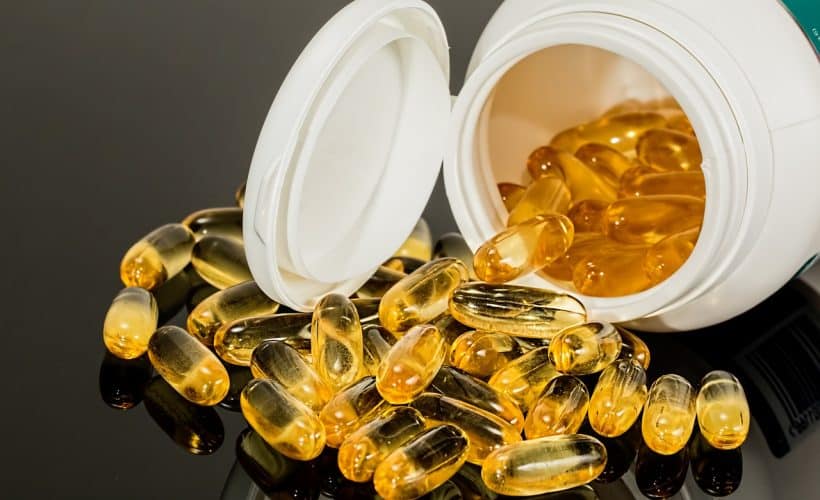 Close-up view of a spilled container of golden capsules or pills, likely dietary supplements or vitamins.