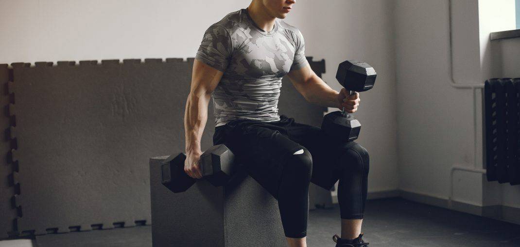 Sports man in the gym. A man performs exercises. Guy in a gray t-shirt