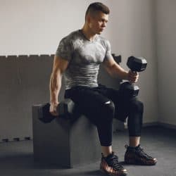 Sports man in the gym. A man performs exercises. Guy in a gray t-shirt