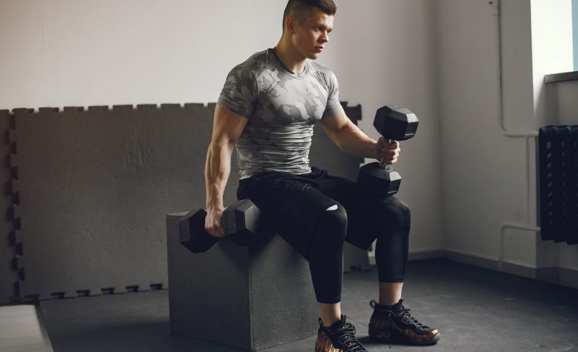 Sports man in the gym. A man performs exercises. Guy in a gray t-shirt