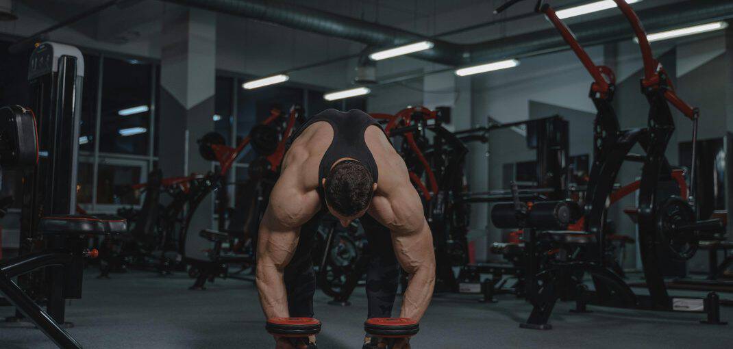 Muscular man lifting weights in a gym surrounded by fitness equipment, highlighting strength training in a professional setting.