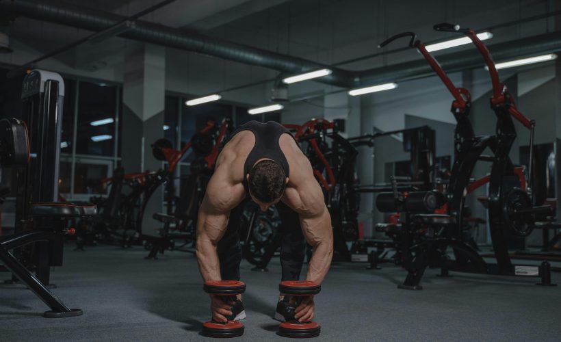 Muscular man lifting weights in a gym surrounded by fitness equipment, highlighting strength training in a professional setting.