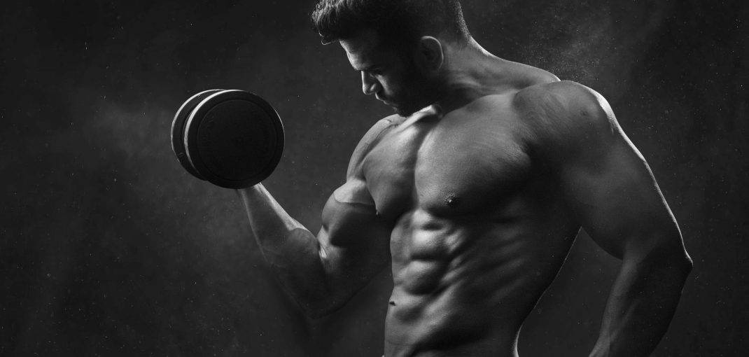 Fit man holding a black dumbbell, emphasizing muscle definition and strength.