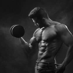 Fit man holding a black dumbbell, emphasizing muscle definition and strength.