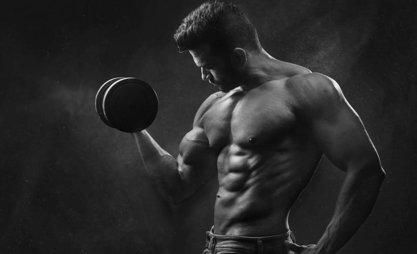 Fit man holding a black dumbbell, emphasizing muscle definition and strength.