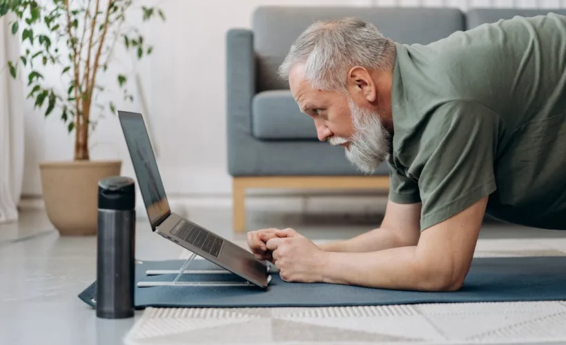 An older man lying on the floor in a plank while using a laptop.