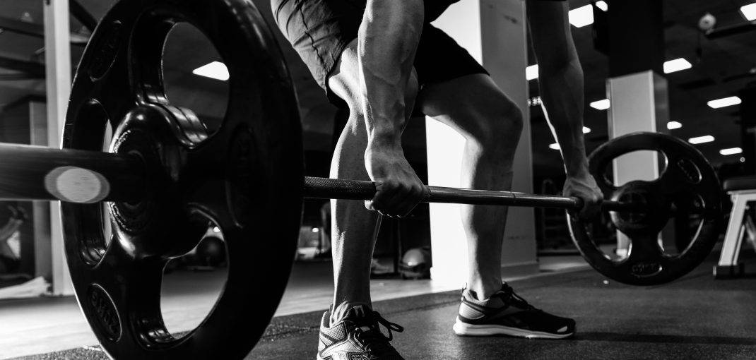 Closeup of weightlift workout at the gym with barbell. Man wearing sportswear clothes.