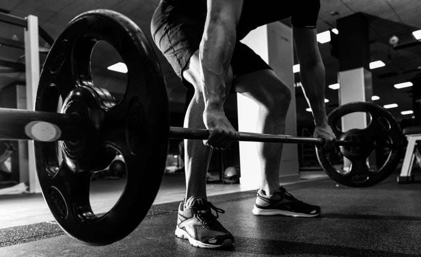 Closeup of weightlift workout at the gym with barbell. Man wearing sportswear clothes.