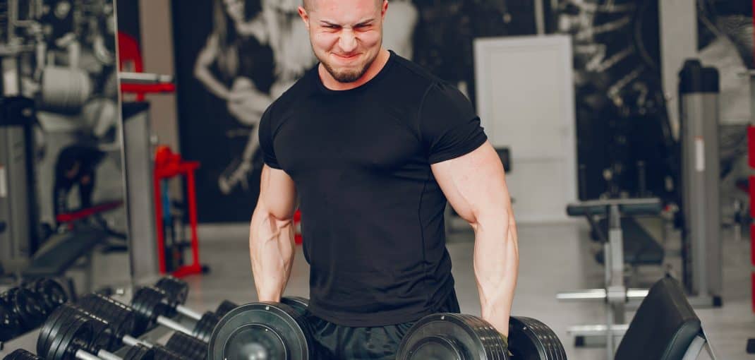 A young and muscular guy in a black t-shirt trains in a gym