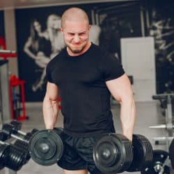 A young and muscular guy in a black t-shirt trains in a gym