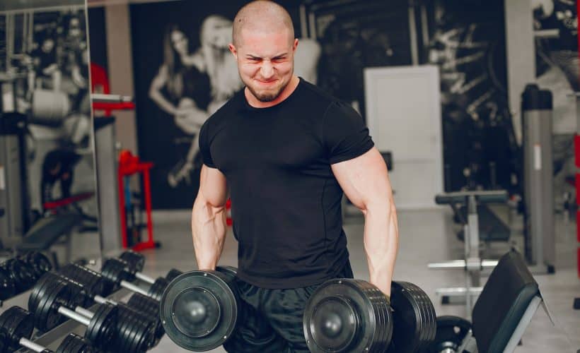 A young and muscular guy in a black t-shirt trains in a gym